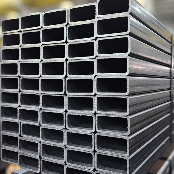 Pilha organizada de tubos retangulares de aço carbono, amarrados e prontos para distribuição em uma área de estoque industrial.