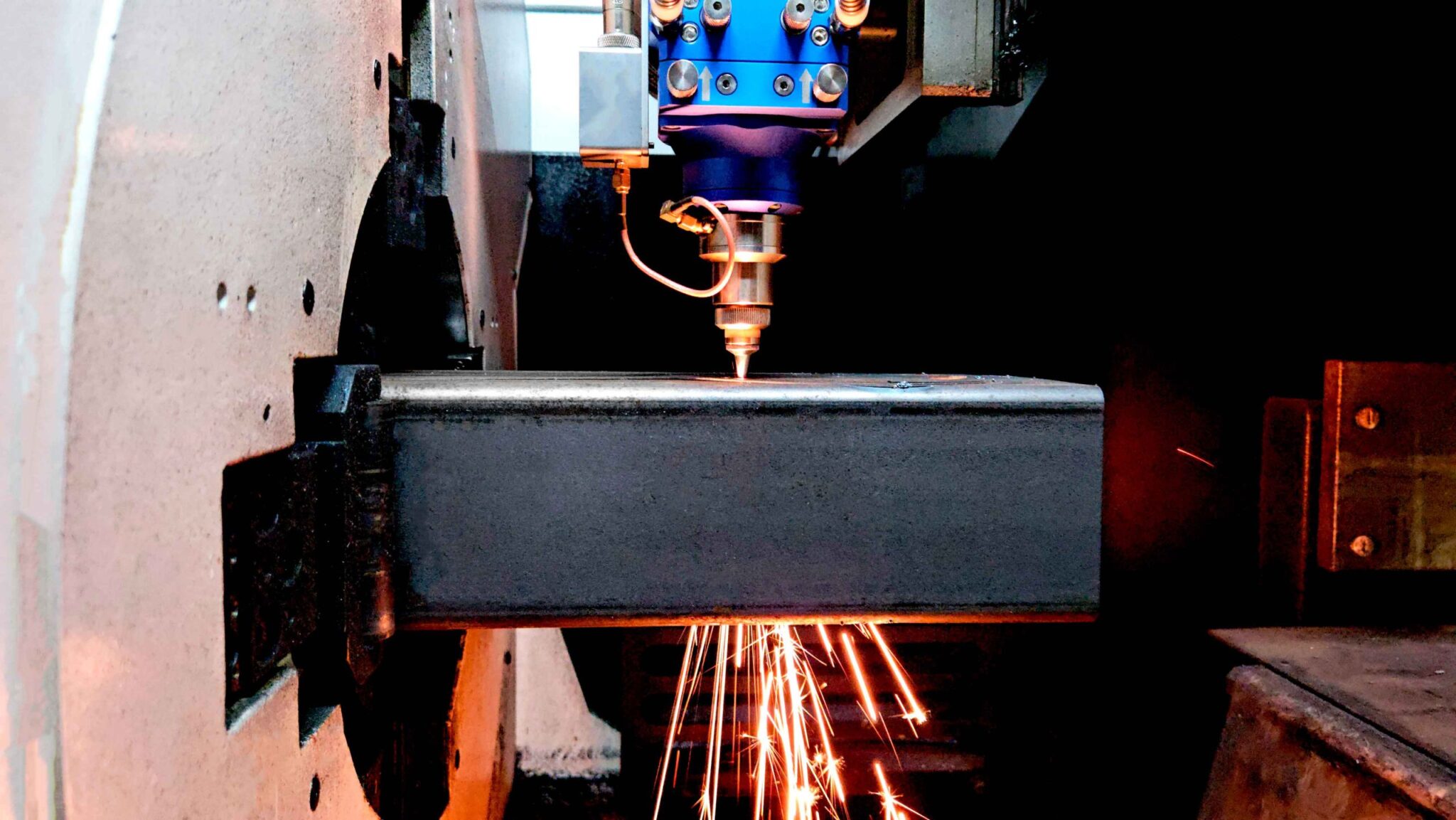 Máquina de corte a laser em operação, cortando uma peça tubular quadrada de aço, gerando intensas faíscas.