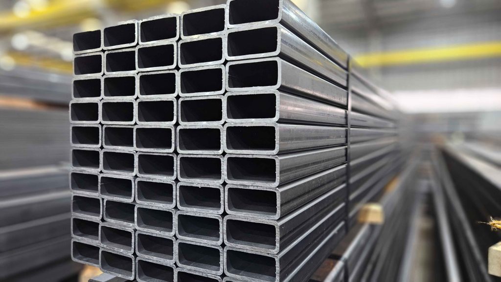 Pilha organizada de tubos retangulares de aço carbono, amarrados e prontos para distribuição em uma área de estoque industrial.