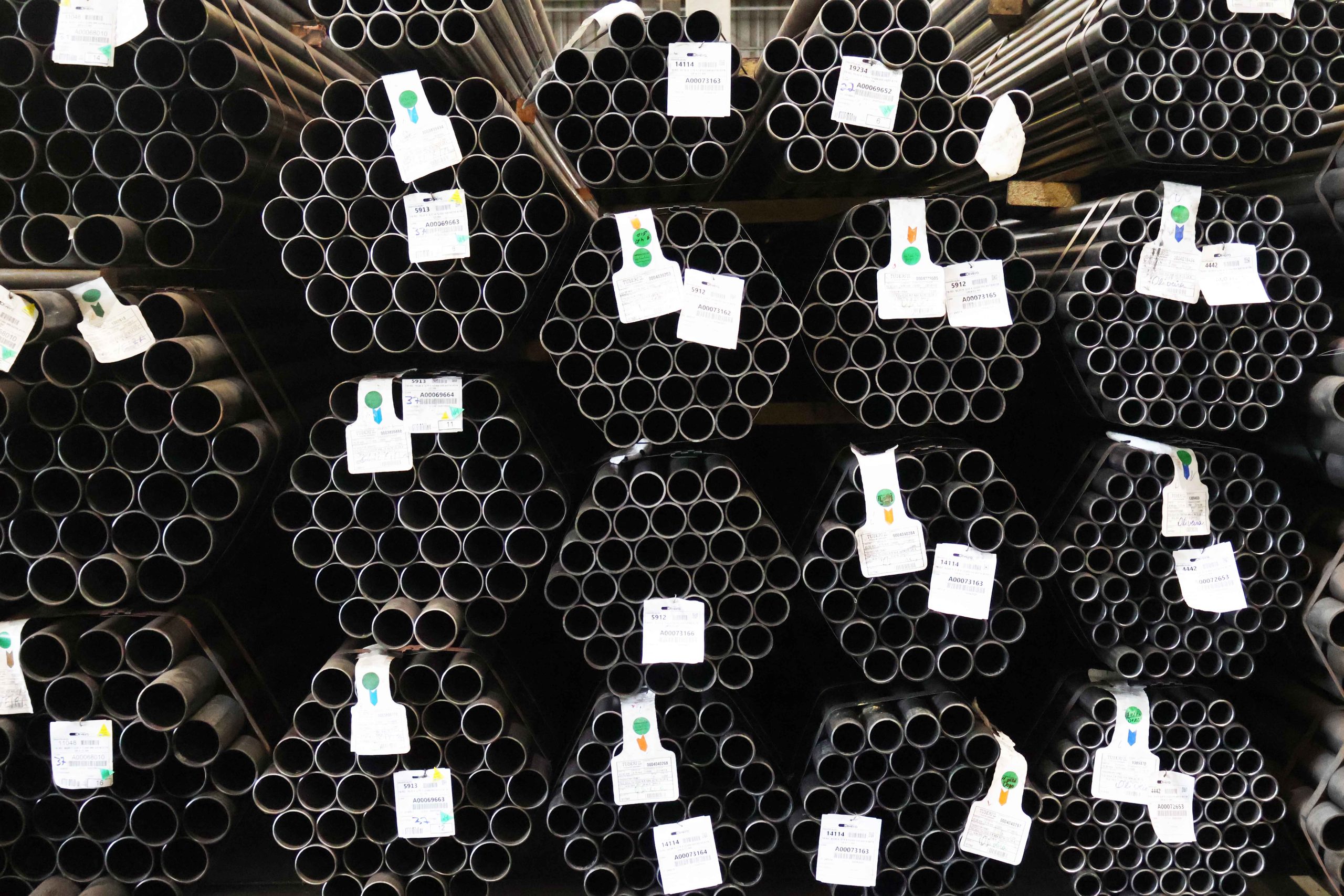 Parede de tubos redondos de aço carbono empilhados no estoque, com diferentes diâmetros e etiquetas de rastreamento.