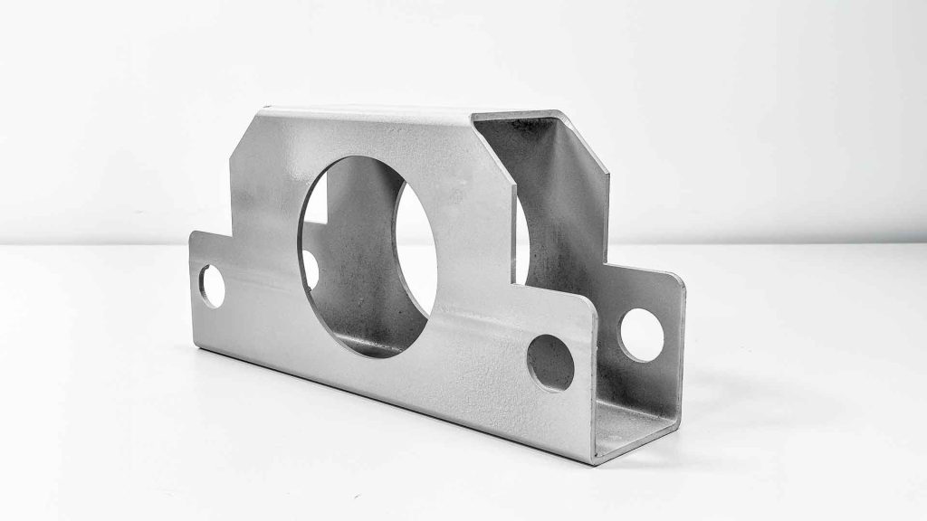 Peça retangular tubular usinada com grande abertura circular central, demonstrando corte e fabricação de precisão.