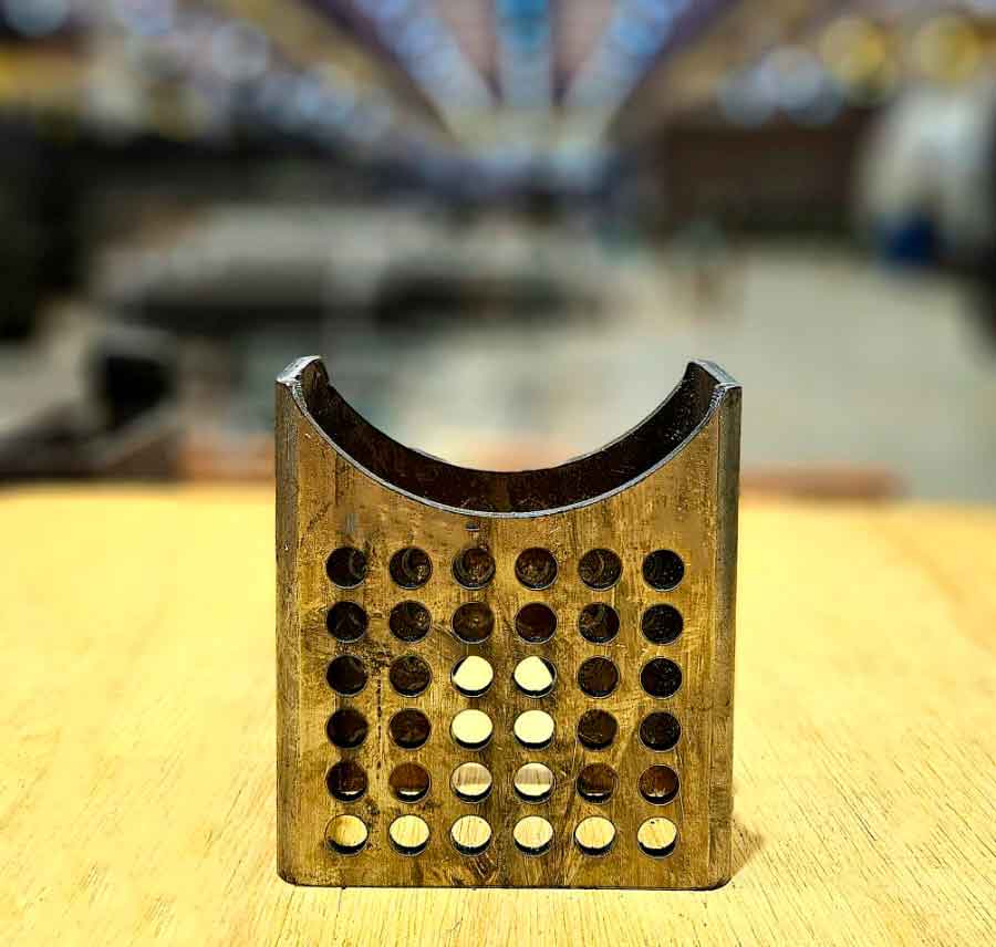 Peça tubular retangular usinada com recortes semicirculares e perfurações circulares, destacando a precisão no corte a laser.