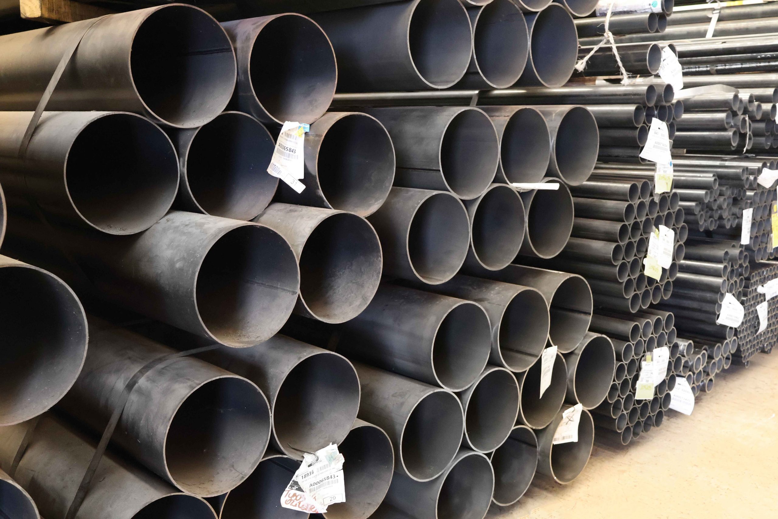 Estoque de tubos de aço carbono redondos, com diferentes diâmetros, prontos para distribuição no estoque industrial.