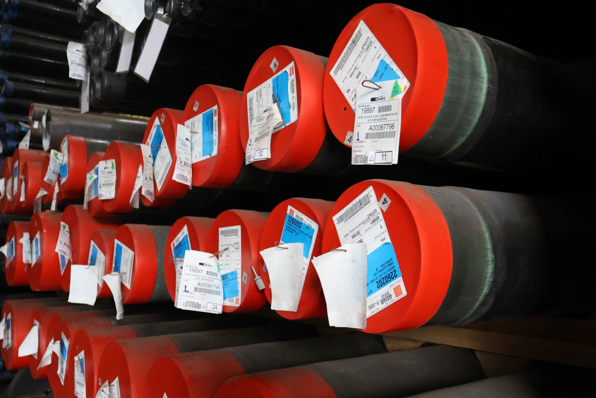 Pilhas de tubo condutor revestido de grande diâmetro com proteções vermelhas nas extremidades e etiquetas de rastreamento de lote.