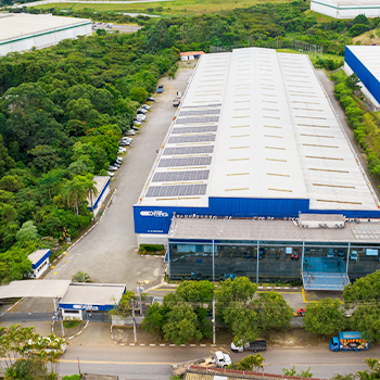 Vista aérea da matriz em Guarulhos da Tubos Oliveira, um grande complexo industrial com telhado branco e painéis solares, cercado por área verde.