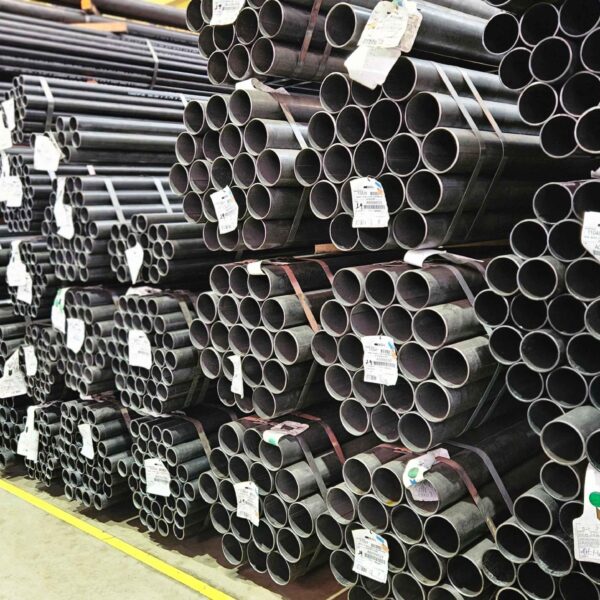 Amplo estoque de tubos redondos de diferentes diâmetros, empilhados e amarrados no galpão industrial.